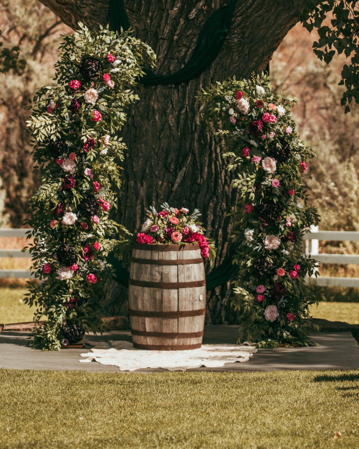 Velvet & Vine faux floral ceremony arch with a whiskey barrel and roses under an oak tree